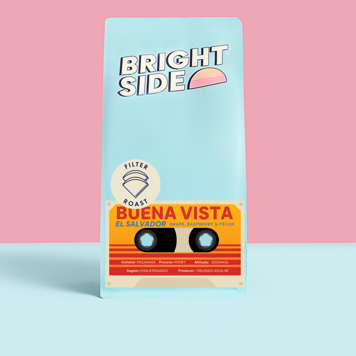 A bag of Bright Side Coffee Roasters 'Buena Vista' coffee stands upright on a light blue surface against a pink background. The bag is light blue with a retro cassette tape graphic in orange, yellow, and red, and features the text 'BRIGHT SIDE', 'FILTER ROAST', and 'BUENA VISTA EL SALVADOR'.